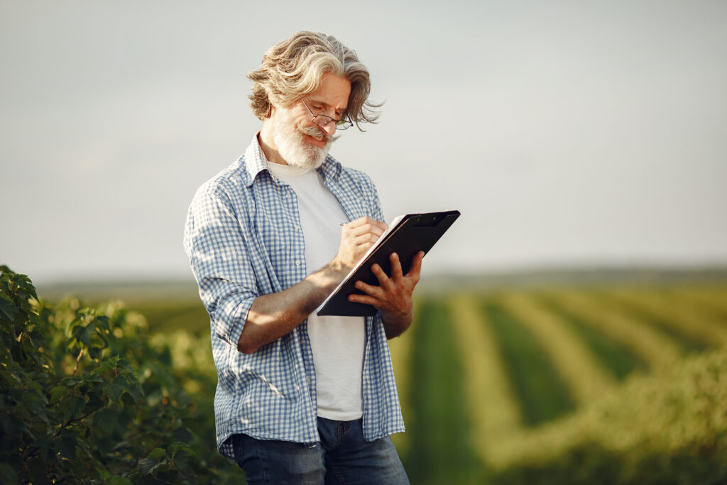 Old farmer in shirt standing on field with notebook