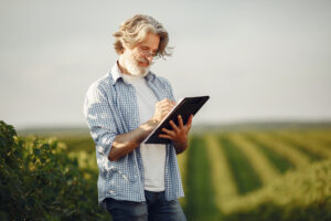 Old farmer in shirt standing on field with notebook