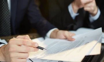 Mao segurando caneta sobre um documento de contrato com outra mao segurando uma folha representando a assinatura de acordos de recuperacao judicial