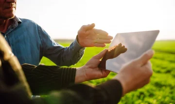 Pessoa visualizando uma Cédula de Produto Rural (CPR) em um tablet ao ar livre, em um campo verde sob luz solar, promovendo negociações e investimentos rurais.